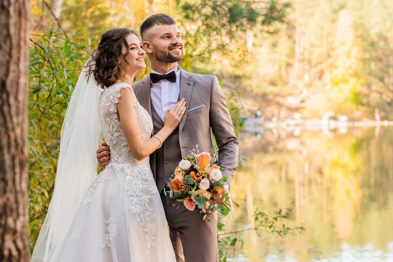 A newlywed couple laughing beside a sunlit tree. Temporary editorial photograph.