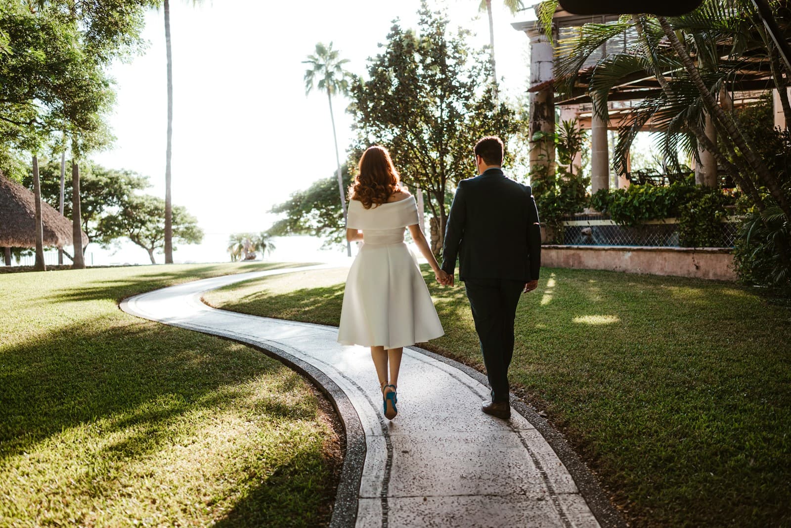 A couple walking down a palm-lined garden path. Temporary editorial photograph.