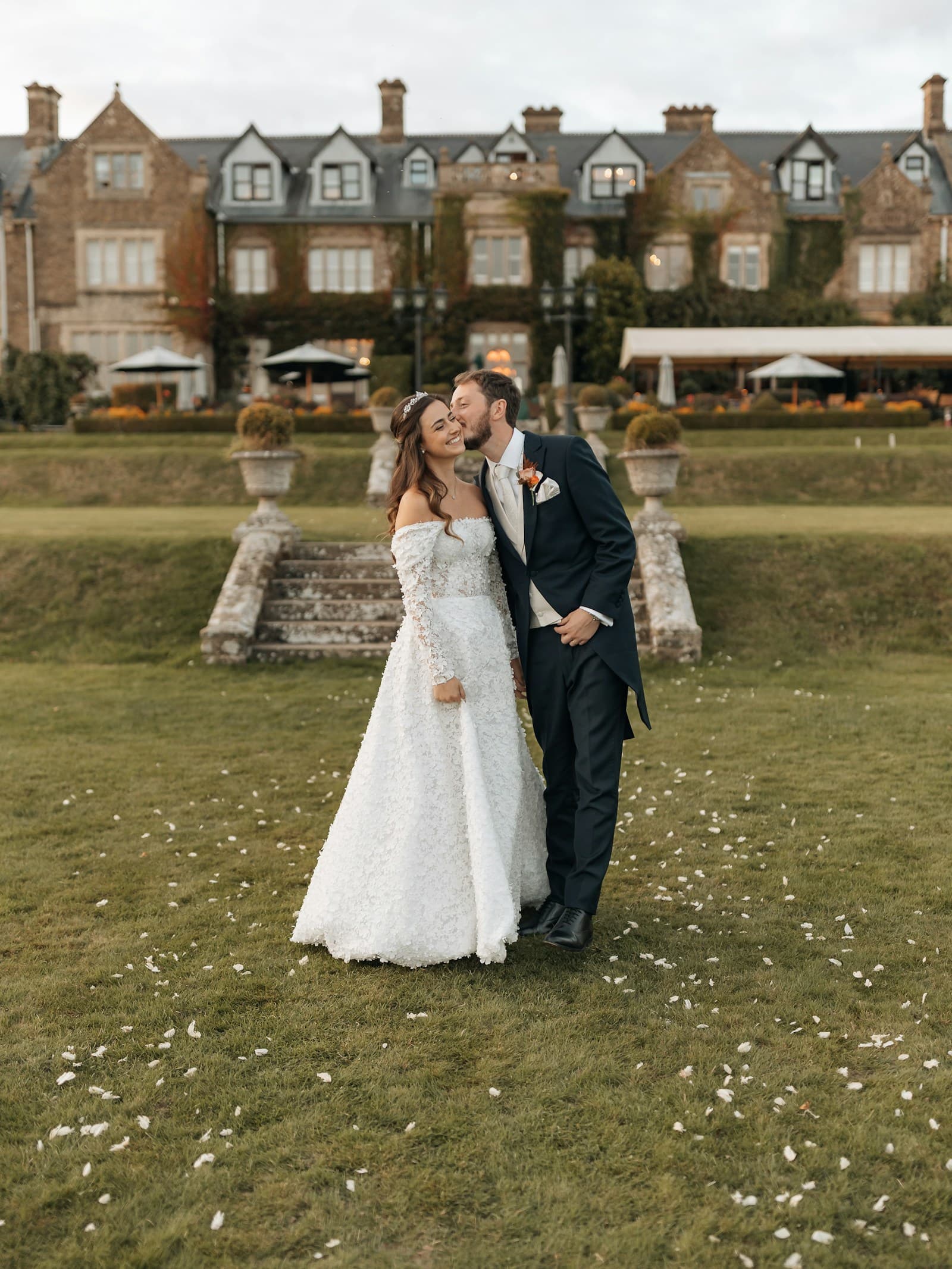 A couple standing on a lawn in front of a historic house. Temporary editorial photograph.