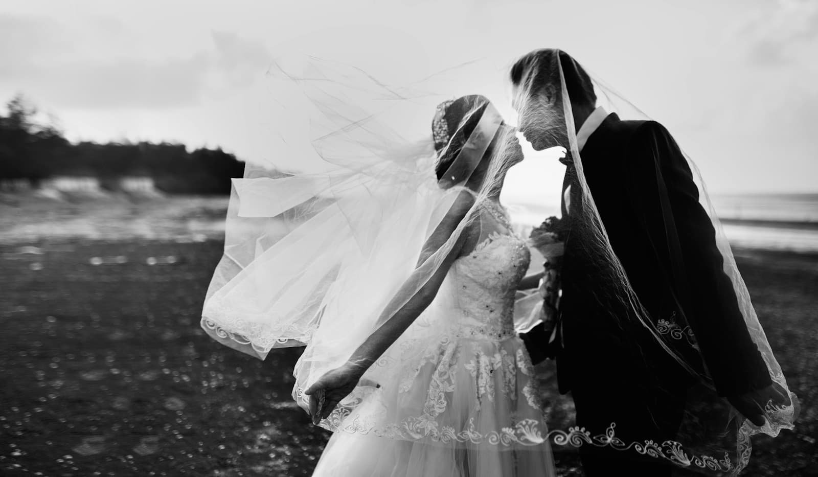 A newlywed couple together beside the sea in black and white. Temporary editorial photograph.