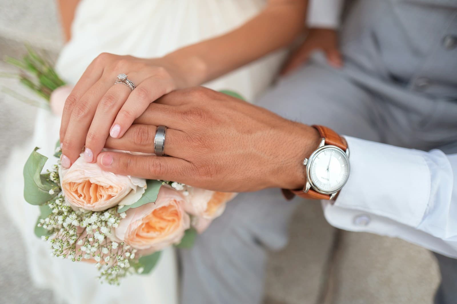 Hands, wedding rings, and a pale bridal bouquet. Temporary editorial photograph.