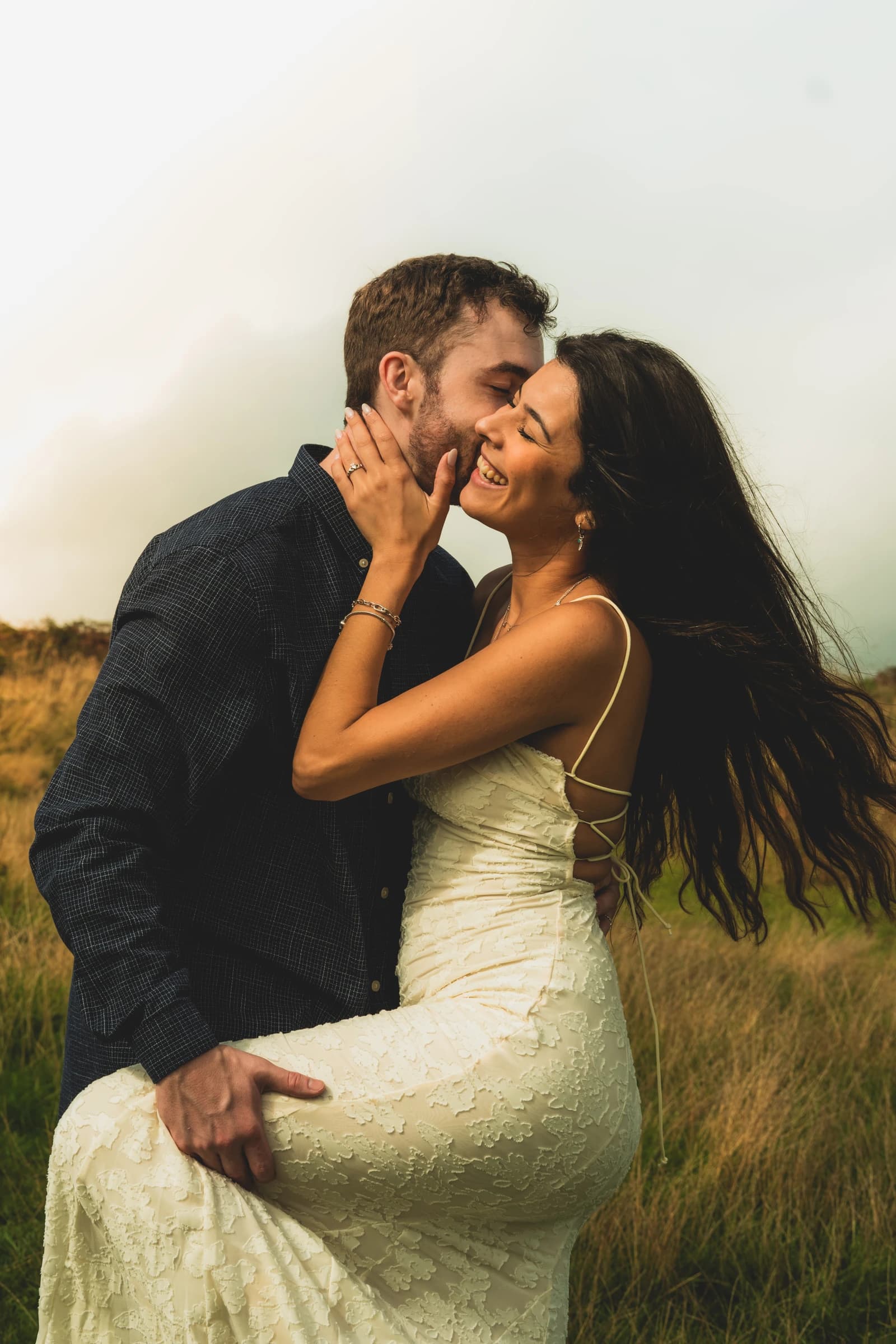 Jamie kissing Alice on the cheek as she smiles in a grassy field.