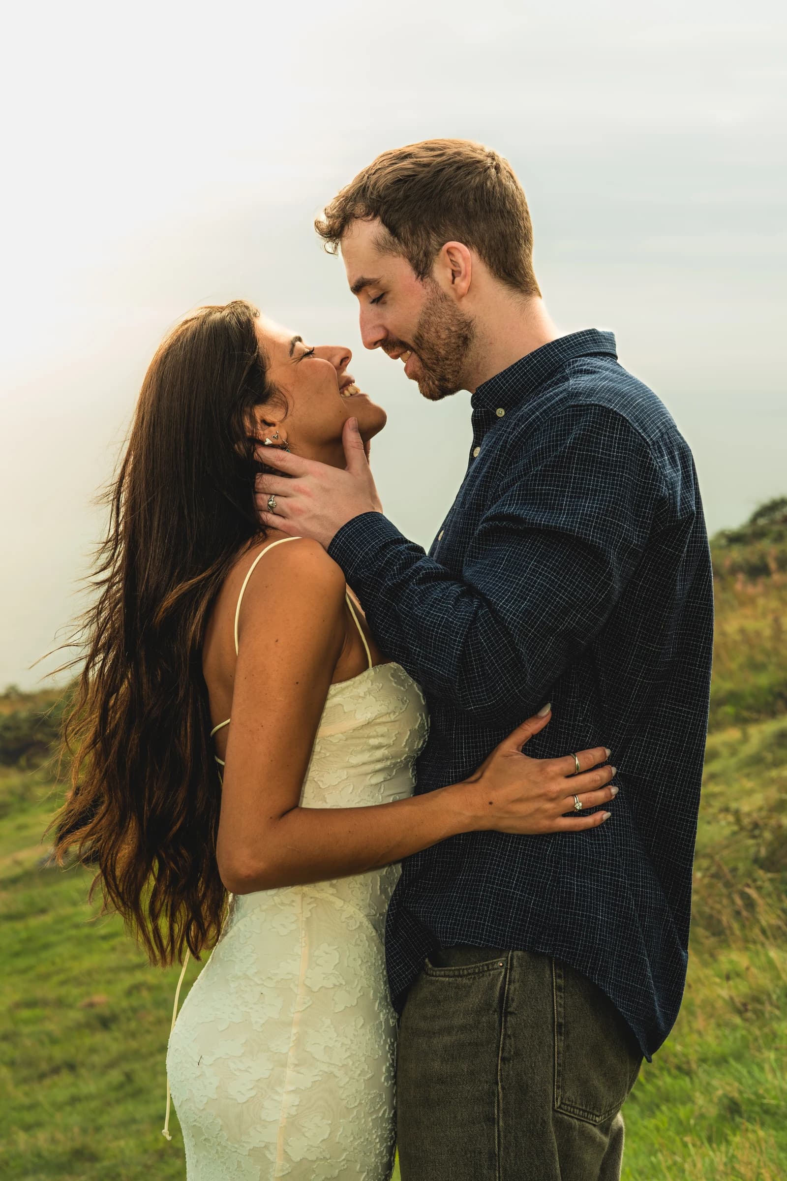 Alice and Jamie smiling at each other in a grassy field, with Jamie holding Alice's chin.