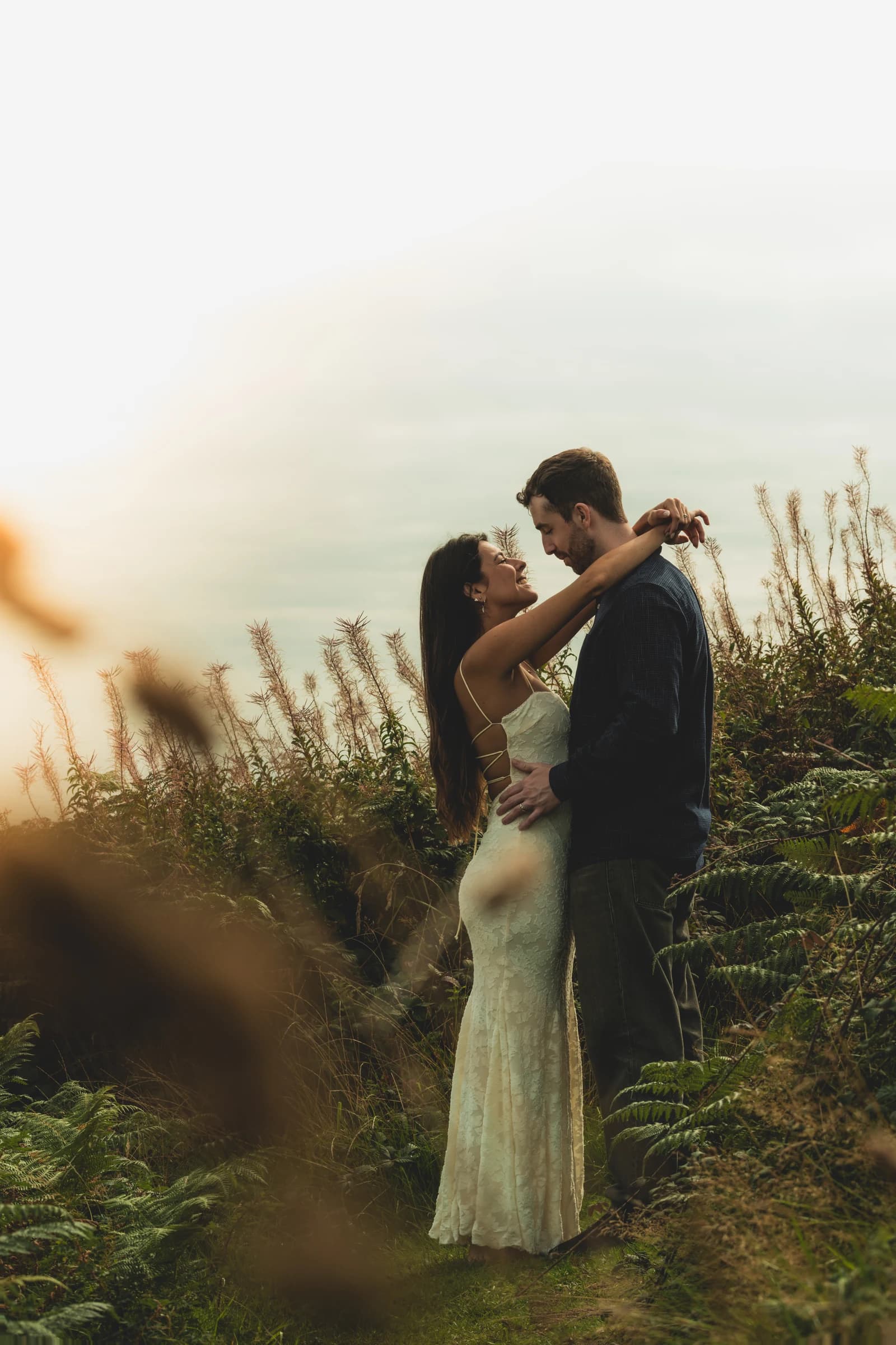 Alice and Jamie embracing among ferns and tall grasses.